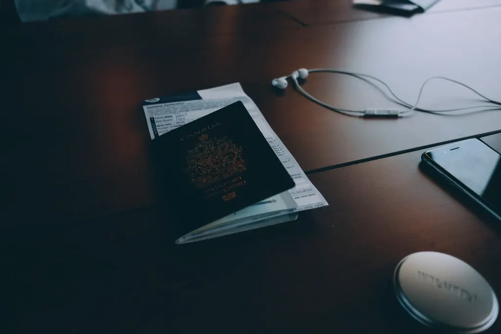 Passaporte e documentos sobre uma mesa de madeira escura, ao lado de fones de ouvido e celular
